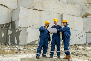 Group of builders discussing sketch on unfolded blueprint during work