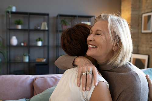 Happy senior woman embracing her friend while they standing in the room, they greeting each other during meeting