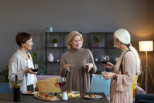 Group of mature women talking to each other and drinking red wine during dinner party at home