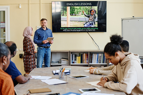 Horizontal shot of multi-ethnic group of migrants attending English language classes doing tasks during lesson