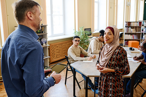 High angle shot of Muslim woman attending classes for immigrants standing in front of teacher trying to speak English