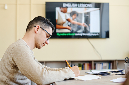 Serious young Middle Eastern man attending English language class writing something in notebook