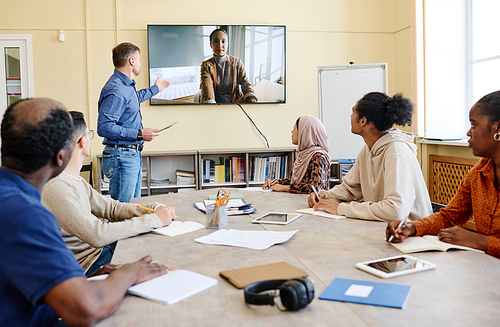 Group of multi-ethnic immigrant students sitting at table watching educational video during English class