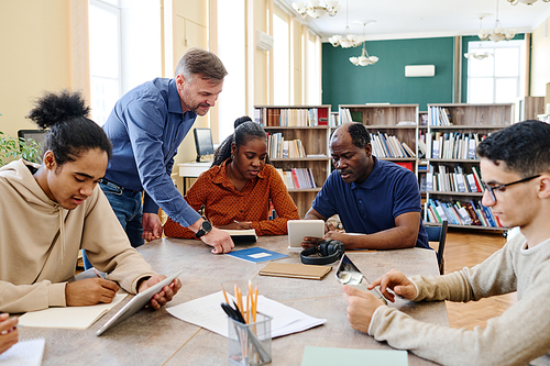 Mature Caucasian English language teacher helping immigrant students to understand task during lesson