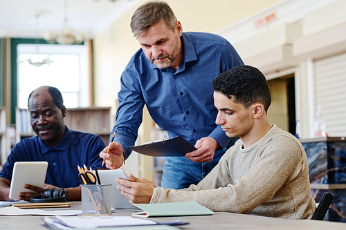 Mature Caucasian man working as English language teacher for immigrants explaining grammar rule to his student