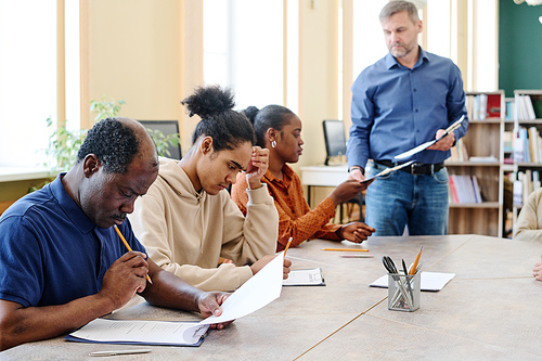 Group of modern Black immigrants attending classes sitting at table finishing doing English grammar test