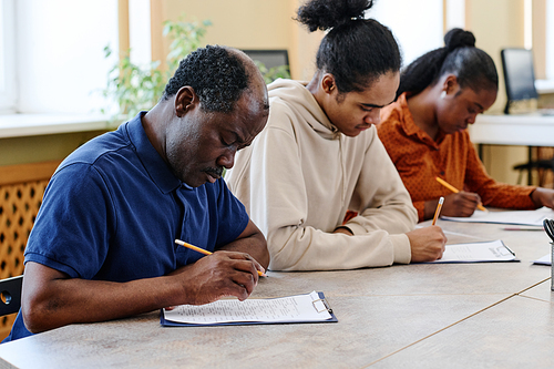 Group of three Black people learning English at school for immigrants sitting at table doing grammar test