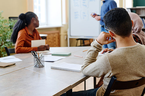 Unrecognizable multi-ethnic man and women sitting at table listening to teacher during English lesson