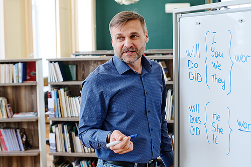 Portrait of Caucasian man working at school standing at whiteboard explaining English grammar rules to his students