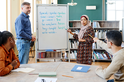 Group of multi-ethnic immigrant students learning English language at school doing task with irregular verbs together