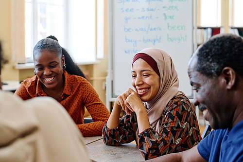 Group of modern immigrants sitting at table having fun laughing at something funny during english lesson