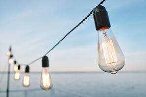 Row of lamps as part of illumination hanging on wire against blue water and sky