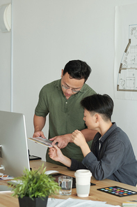 Two young designers of Asian ethnicity discussing color samples for new project at working meeting in office