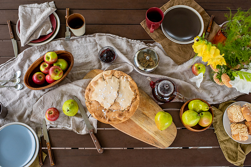 Overview of rectangular wooden table served with homemade pie and buns, fresh fruits and flowers from garden and tea with jam and sugar