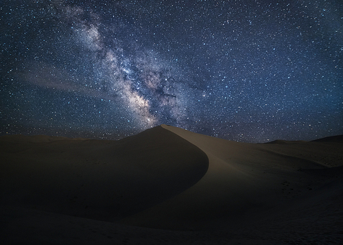 The heavenly Milky Way slowly fills the desert with a graceful curve that divides it into two sides.