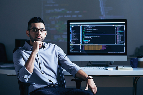 Indian professional programmer sitting at his table with big monitor