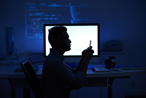 Silhouette of software developer reading text message aganst glowing computer screen