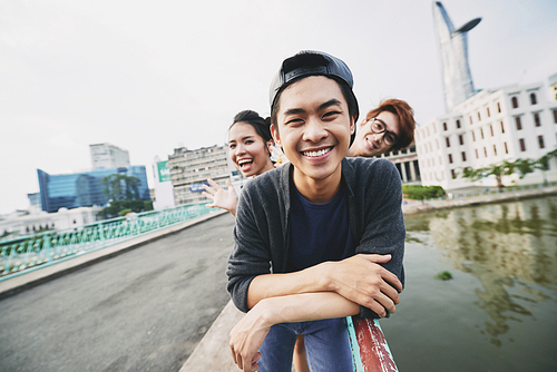 Portrait of handsome young man  with toothy smile, his friends standing behind him and posing for photography