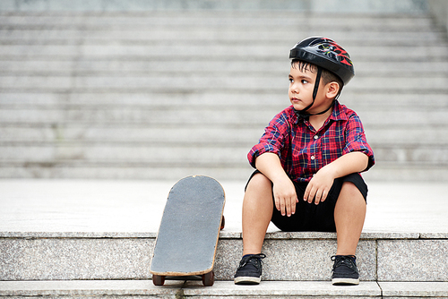 Tired boy sitting on stairs next to his skateboard