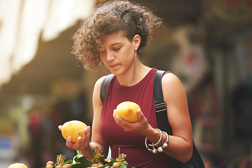 Pensive woman choosing yellow mangos at farmers market