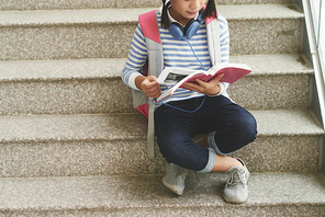 Cropped image of schoolgirl sitting on stairs and reading a book