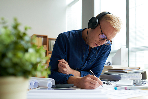 Engineer in glasses and headphones drawing blueprint