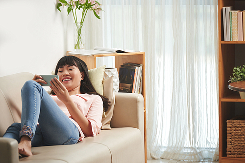 Young Vietnamese woman laughing when using application on smartphone