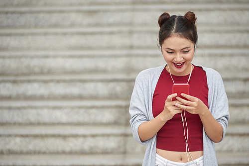 Happy young woman texting to friends when standing in street