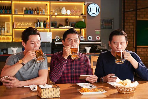 Group of Vietnamese mature men enjoying tasty fresh beer in the bar