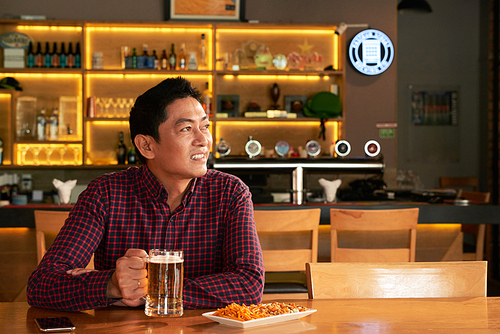 Asian man enjoying beer and snacks in sports bar