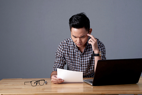 Waist-up portrait of concentrated Asian financial manager doing paperwork while sitting at office desk