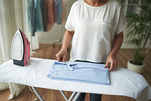 Hands of woman folding blue shirt after ironing
