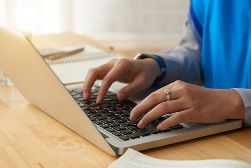 Close-up view of unrecognizable young woman sitting at table and working on laptop