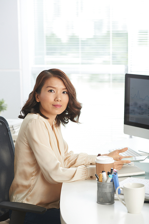 Asian businesswoman sitting at office desk with tablet computer in her hands and 