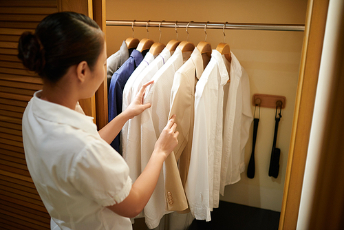 Chambermaid checking clothes in closet of guest