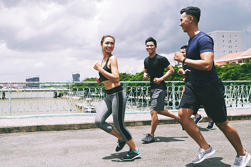Young cheerful people running behind pretty fit woman