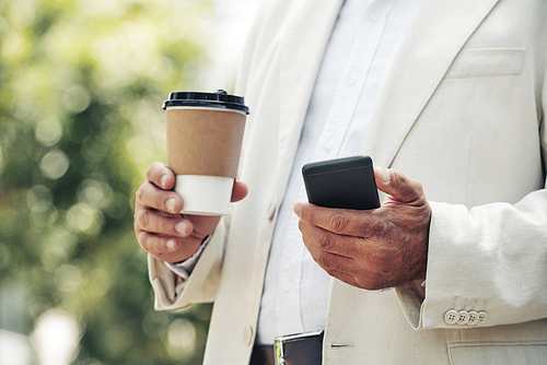 Take-out coffee and smartphone in hands on man