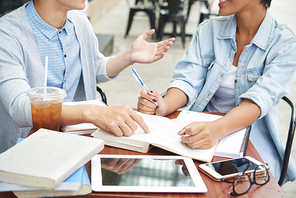 Unrecognizable college students sitting at cafe table covered with textbooks and copybooks and preparing for exam, close-up shot