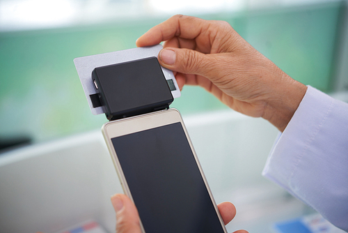 Card reader device attached to smartphone in hands on pharmacist