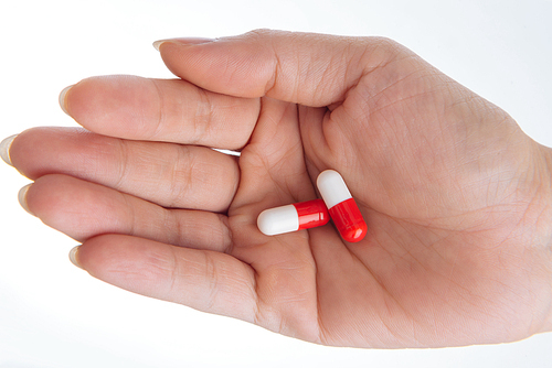 Close-up shot of unrecognizable woman holding two pills in hand, isolated on white