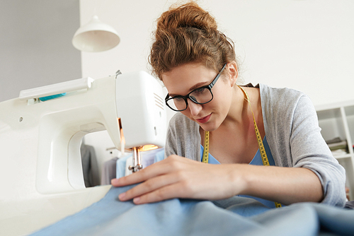 Young woman in glasses busy with work on sewing machine