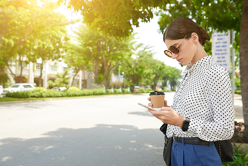Stylish business woman standing in the street and reading text message on her smartphone