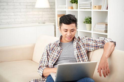 Handsome Asian young man relaxing on sofa with laptop