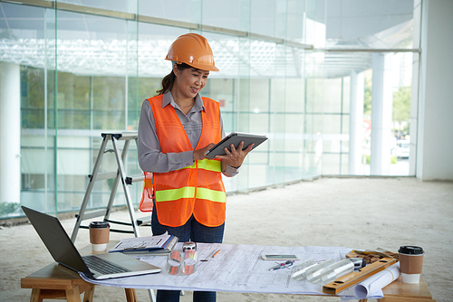 Smiling female construction worker reading something on tablet computer