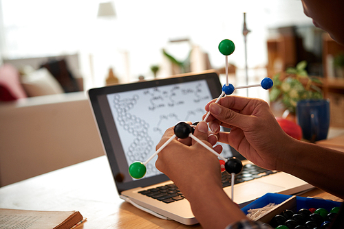 Hands of student assembling molecular model according to directions on laptop screen