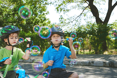 Brothers in sport helmets blowing soap bubbles outdoors