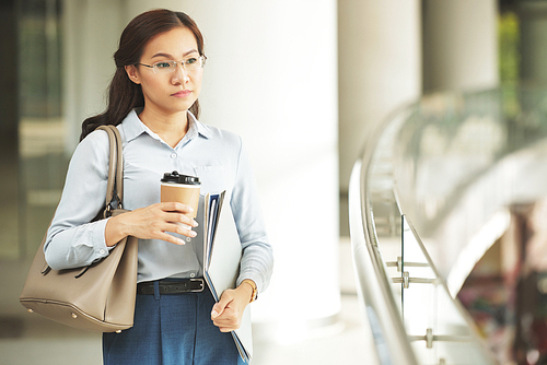 Pensive Asian business woman with coffee and folders