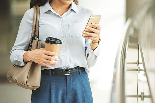 Copped image of business woman with coffee cup checking her smartphone