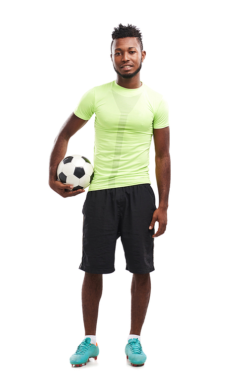 Full length portrait of handsome Nigerian soccer player  with toothy smile while holding ball in hand, isolated on white