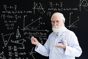 Waist-up portrait of elderly professor of mathematics with bushy beard standing at blackboard and explaining learning material to students